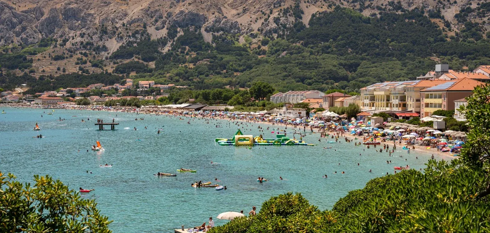 The long pebble beach of Baska on the island of Krk with the campsite belt and bare mountains behind, Croatia