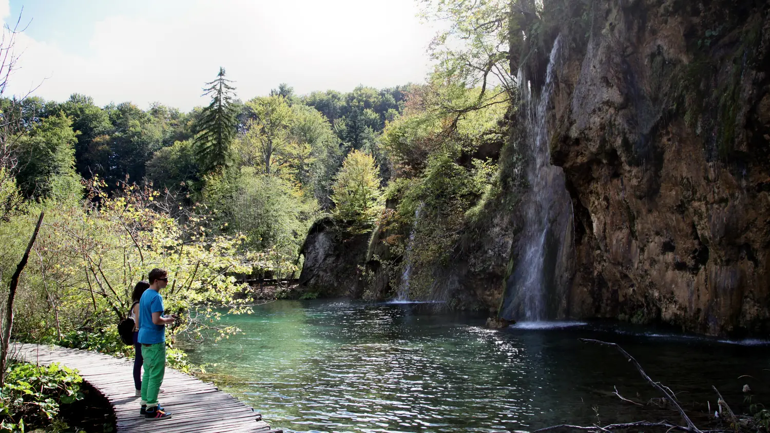Wooden boardwalk beside a waterfall and a turquoise pool in the Lower Lakes of Plitvice Lakes National Park, Croatia