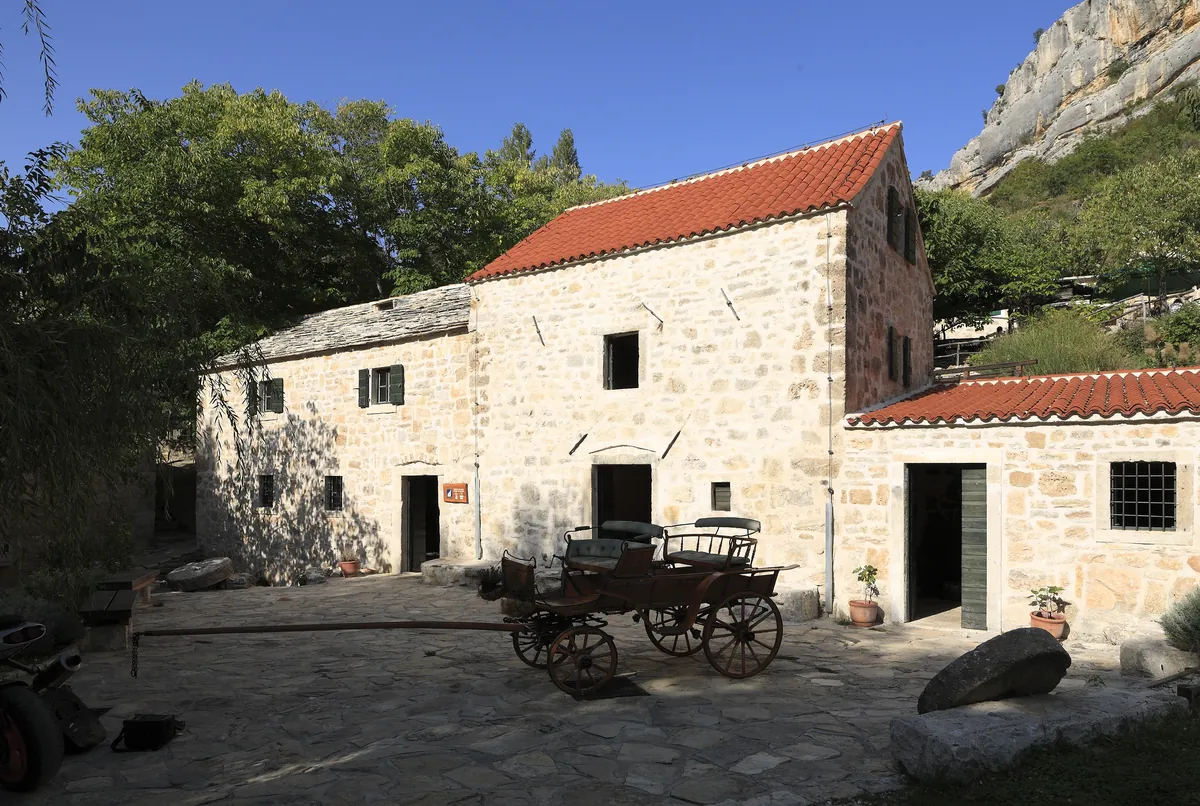 Restored stone watermills with a wooden cart in the courtyard at Roški Slap, Krka National Park, Croatia