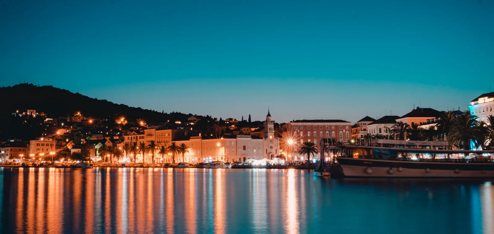 The waterfront of Split lit up at dusk seen from the water, with Marjan hill in silhouette, Croatia