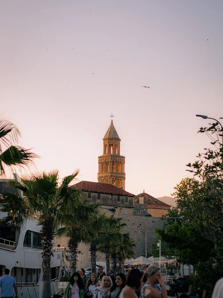 The cathedral bell tower of Split glowing at sunset above the old town walls and palm trees, Croatia
